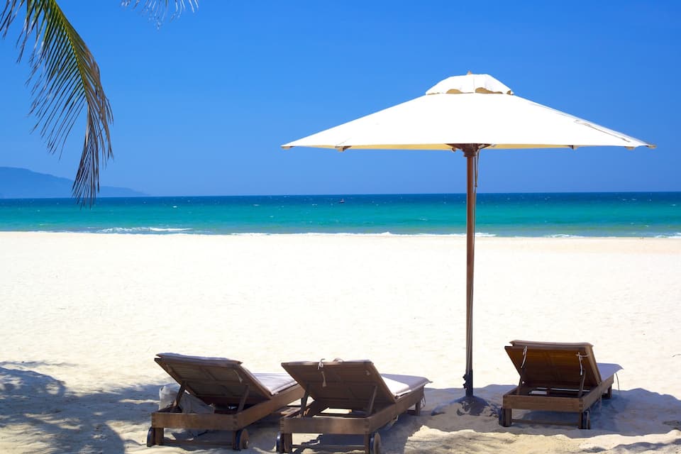 A beach with two wooden sun loungers and a white umbrella.