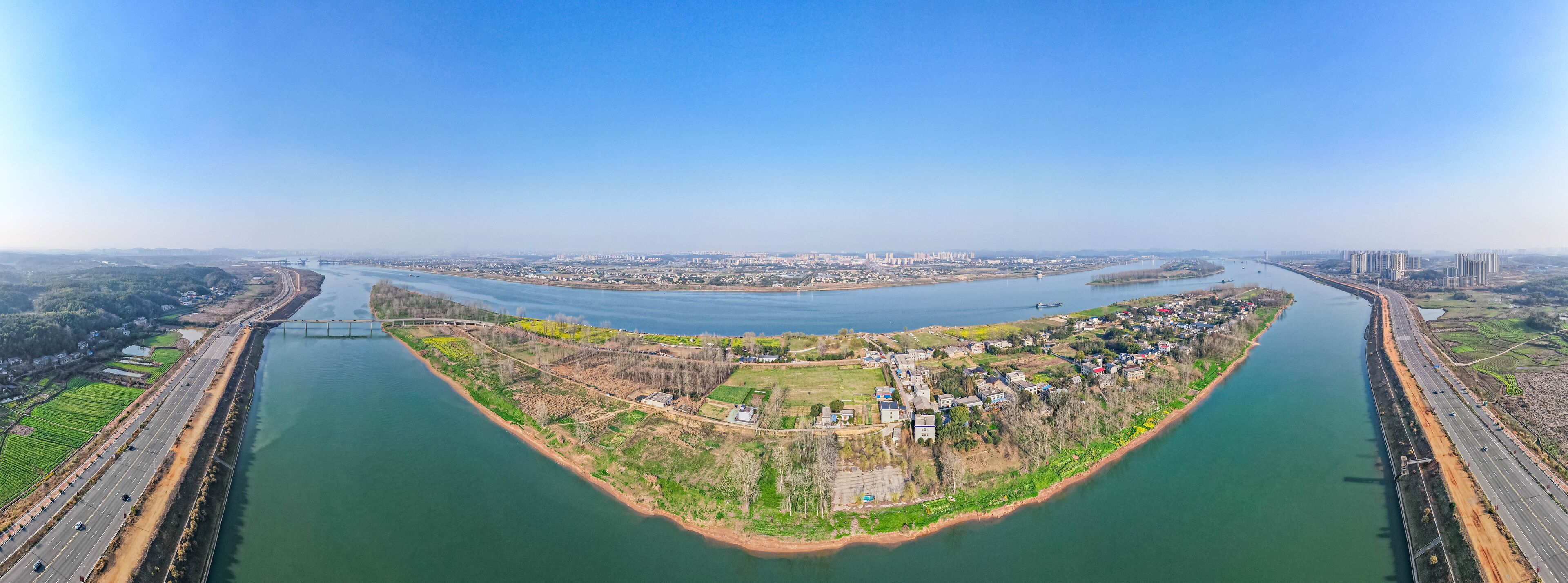 A river meandering through a town with a bridge and a highway parallel to it.