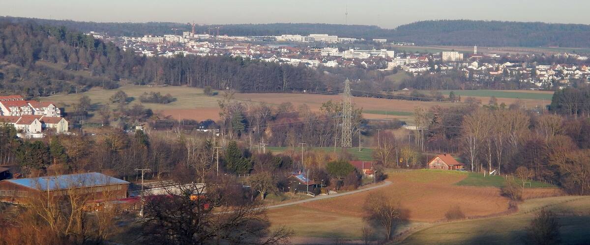 A town with a mix of residential and industrial buildings, surrounded by fields and forests.