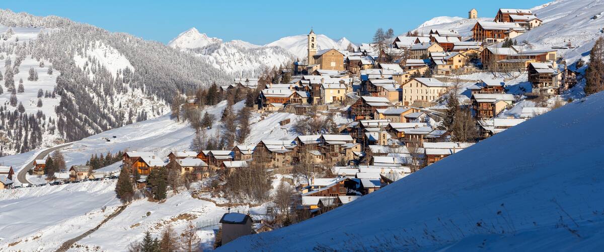 A snow-covered village nestled in a mountainous region with wooden houses and a church.