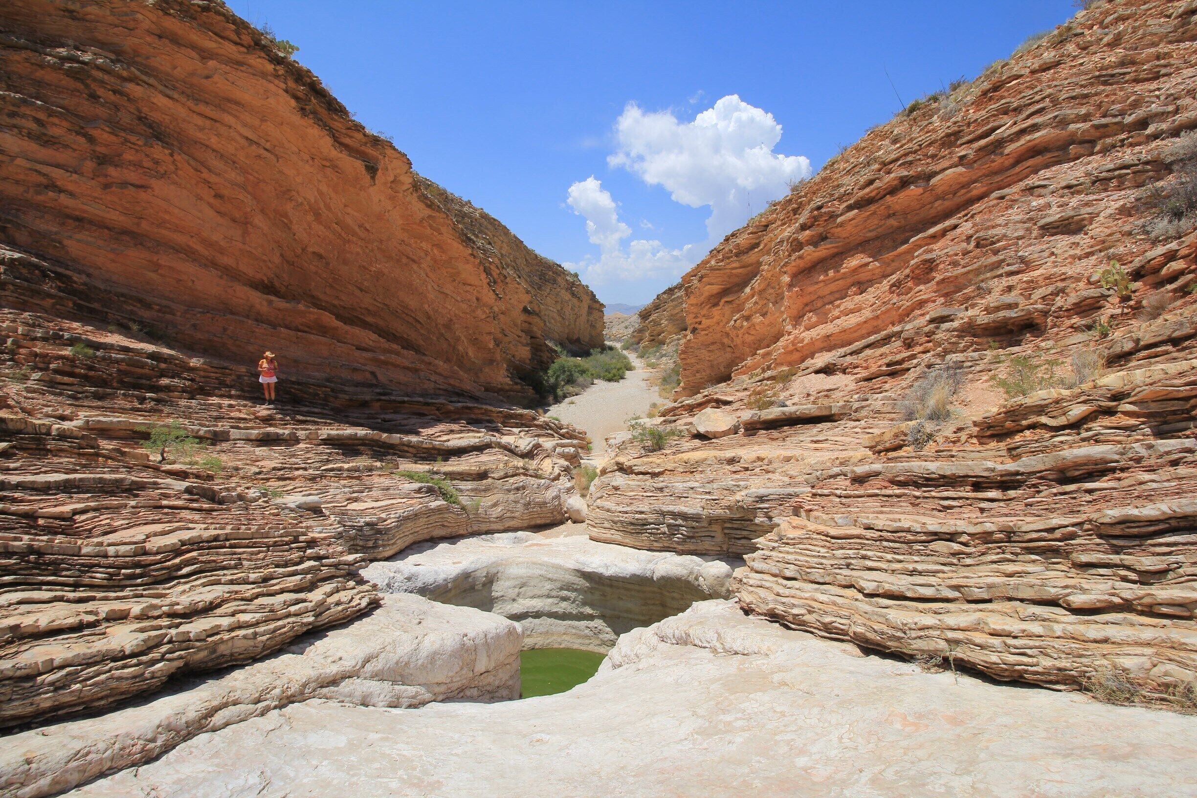 A canyon with layered rock formations and a small green pool.