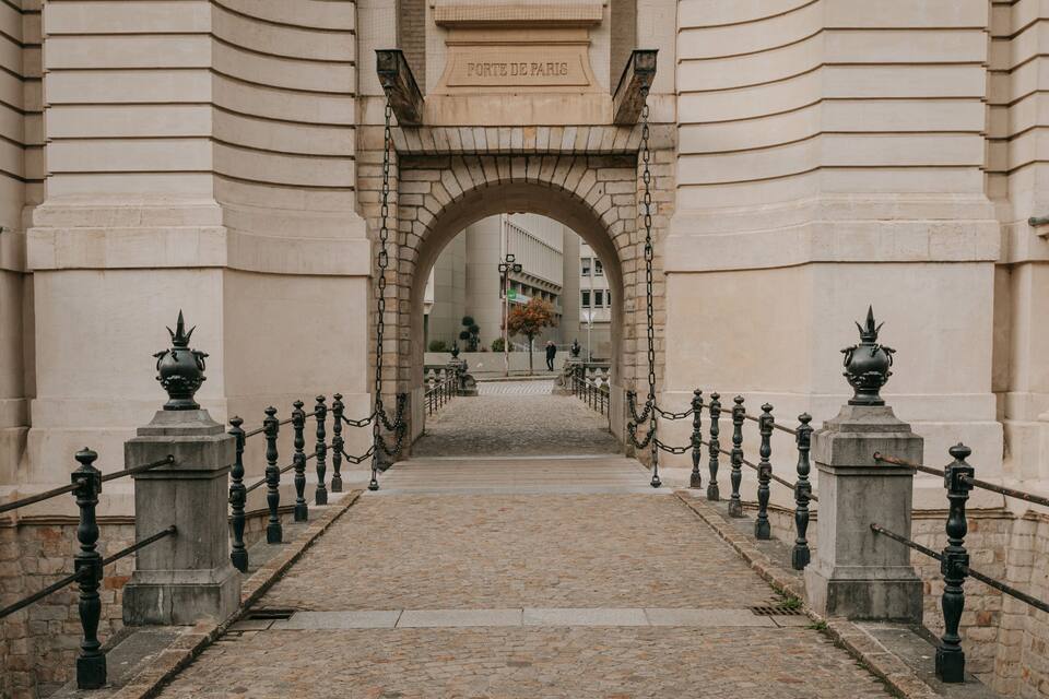 Un sentier pavé de pierres menant à travers une arche en pierre sur laquelle est gravée l’inscription « PORTE DE PARIS ».