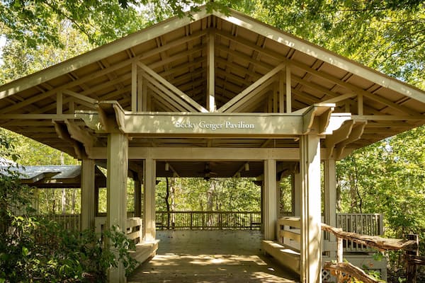 A wooden pavilion named Becky Geiger Pavilion surrounded by lush greenery.