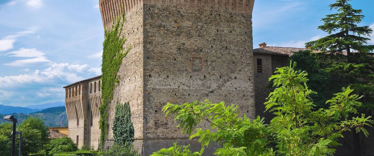 A historic stone tower with crenellations, surrounded by lush greenery and a clear sky.