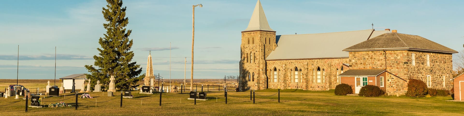 A stone church with a tall steeple and a large tree in front.