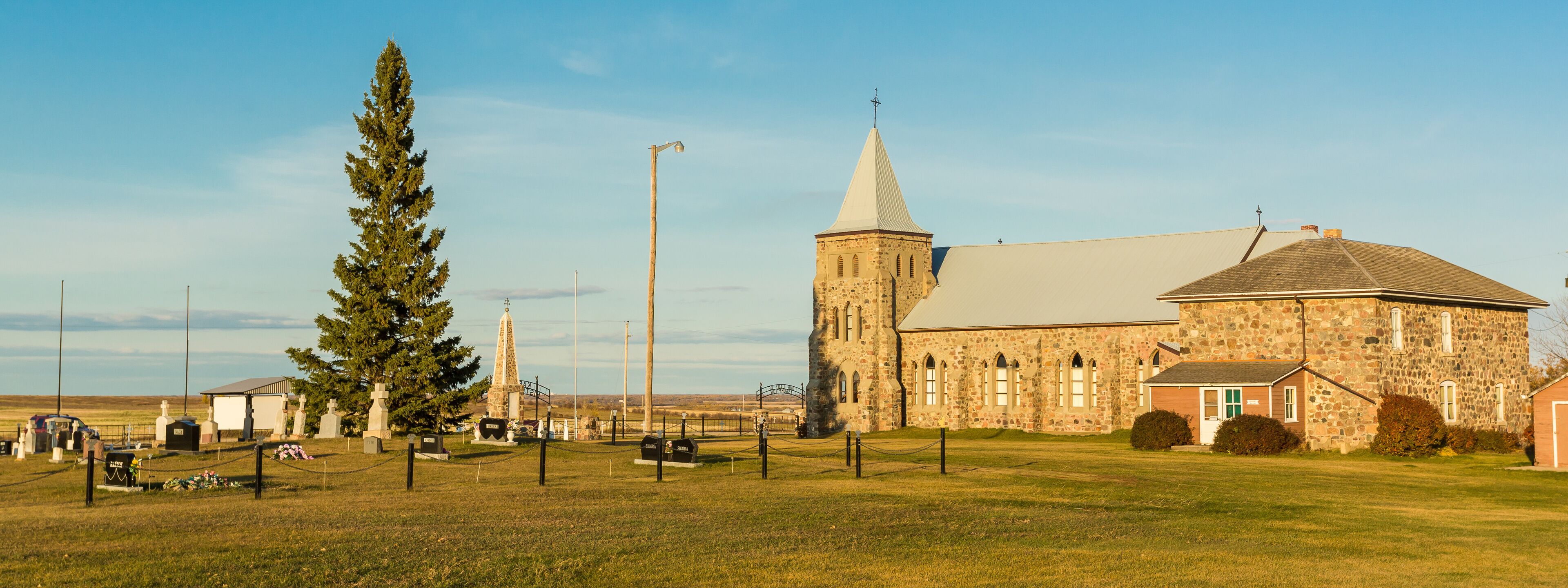 A stone church with a tall steeple and a large tree in front.