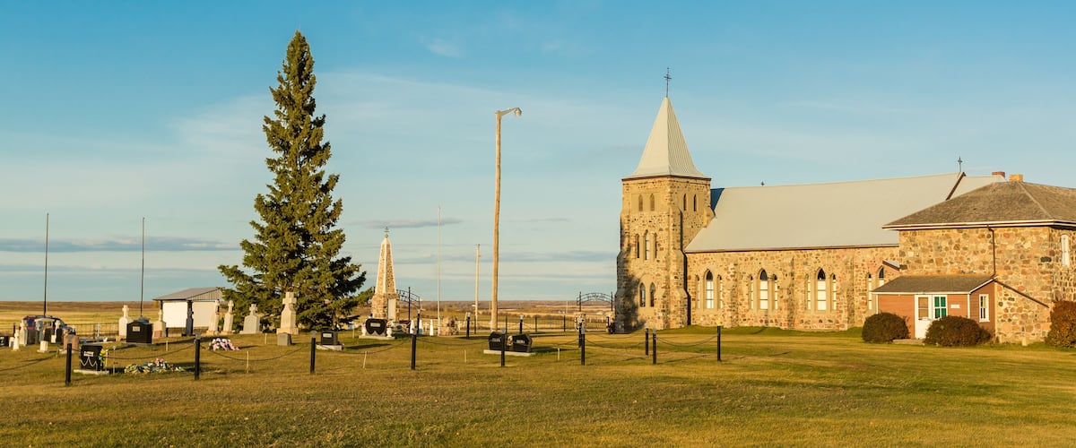 A stone church with a tall steeple and a large tree in front.