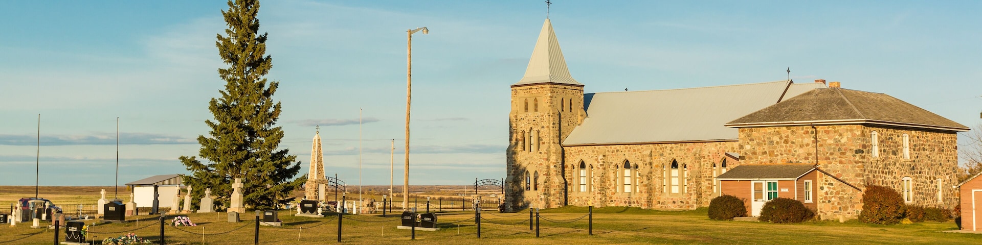 A stone church with a tall steeple and a large tree in front.