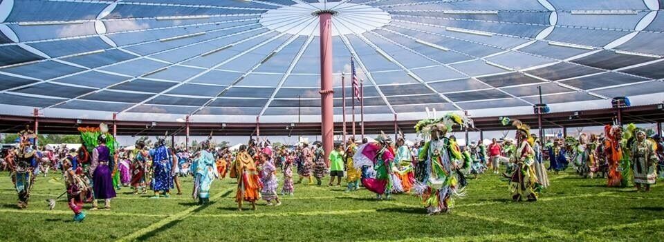 A large, open-air structure with a glass ceiling, surrounded by people in colorful traditional costumes.