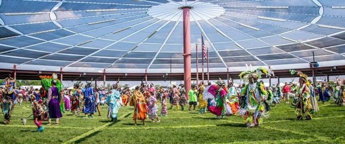 A large, open-air structure with a glass ceiling, surrounded by people in colorful traditional costumes.