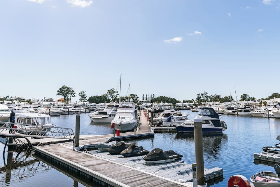A marina with various boats docked, a wooden pier, and a clear blue sky.