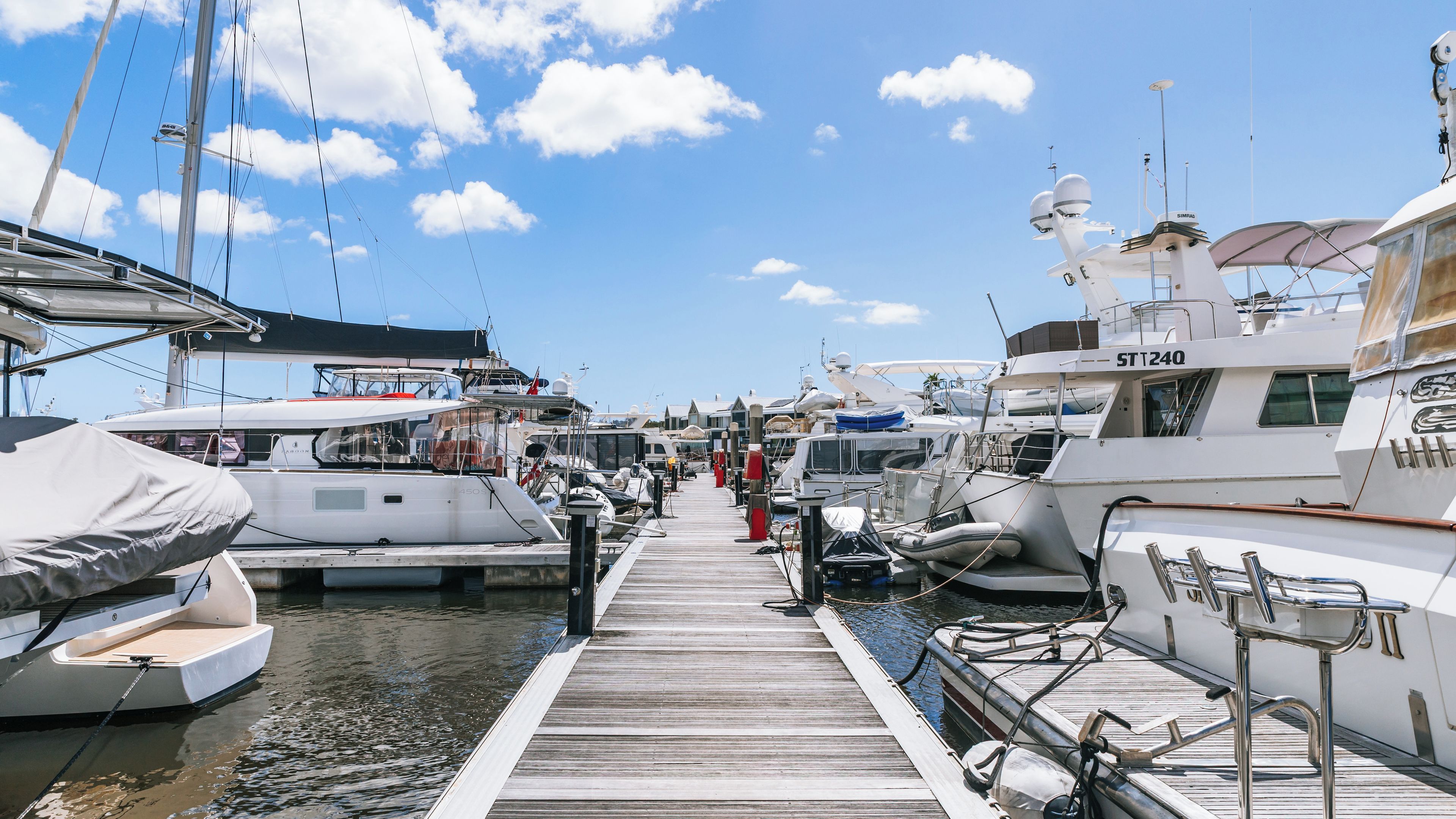 A marina with multiple yachts docked along a wooden pier under a clear blue sky.