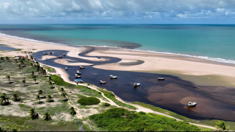 Un paysage côtier avec une rivière sinueuse, des plages de sable et quelques bateaux dispersés.