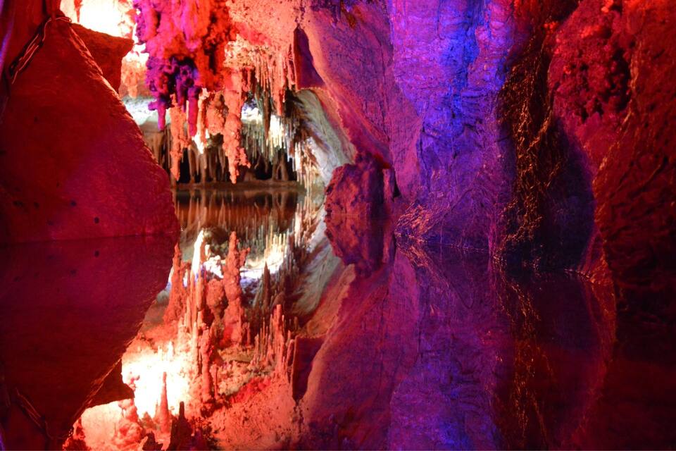 A cave with stalactites and stalagmites, illuminated by colorful lights.