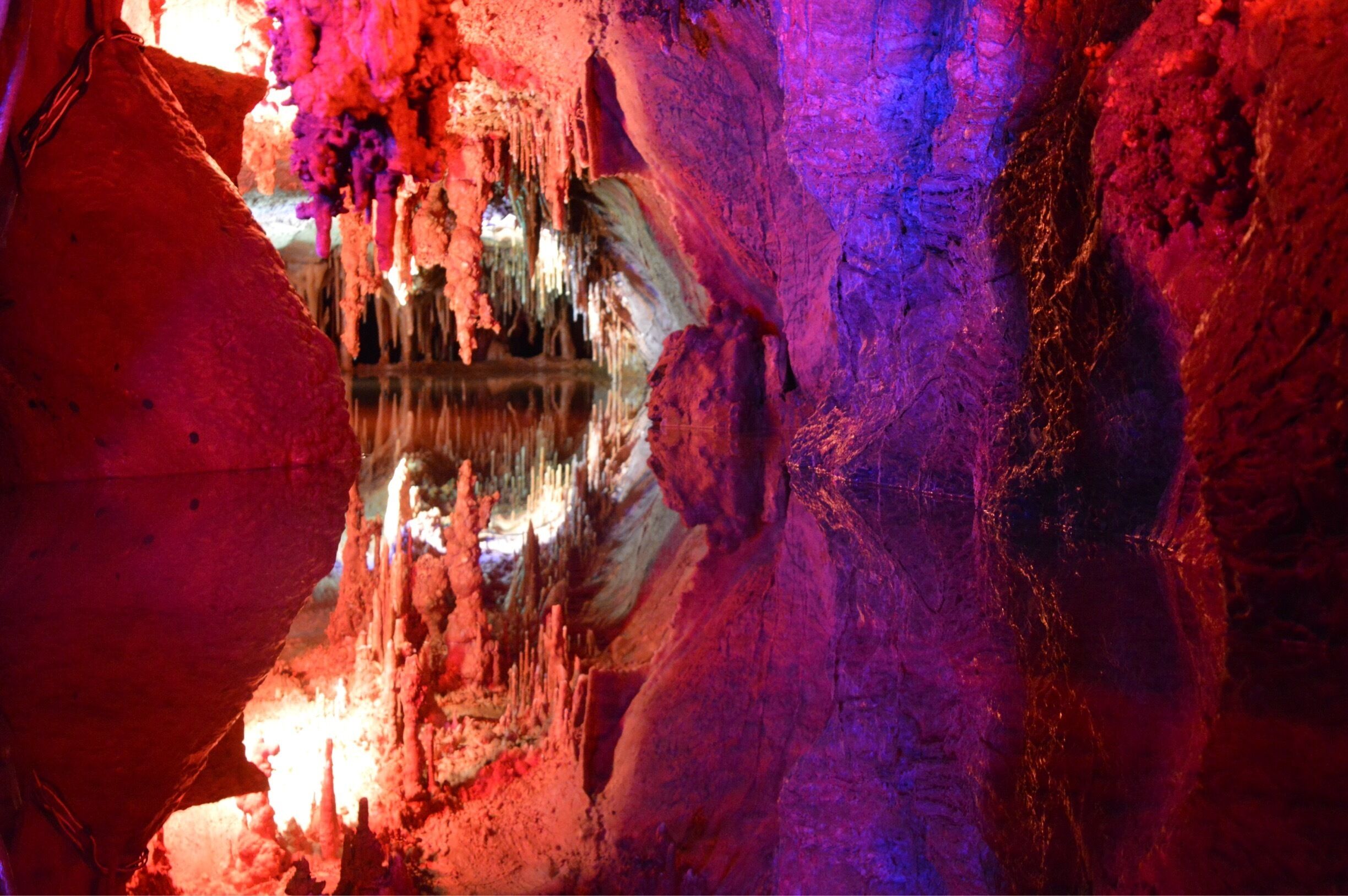 A cave with stalactites and stalagmites, illuminated by colorful lights.