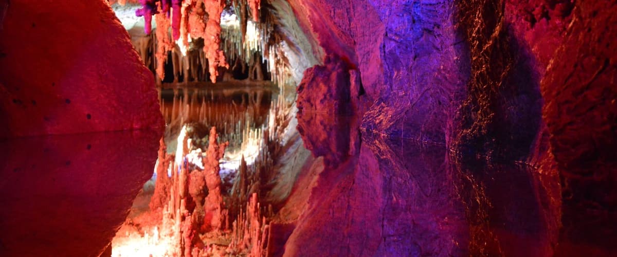 A cave with stalactites and stalagmites, illuminated by colorful lights.