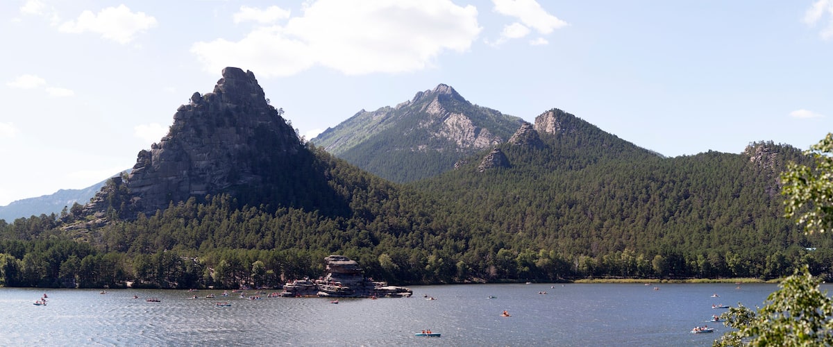A lake surrounded by mountains and a rocky island with people kayaking.