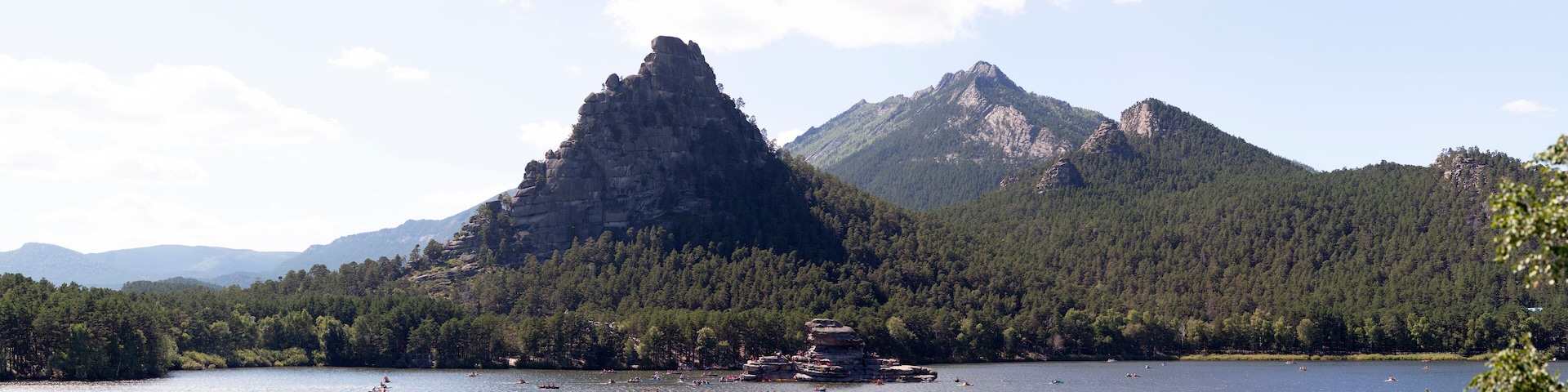 A lake surrounded by mountains and a rocky island with people kayaking.