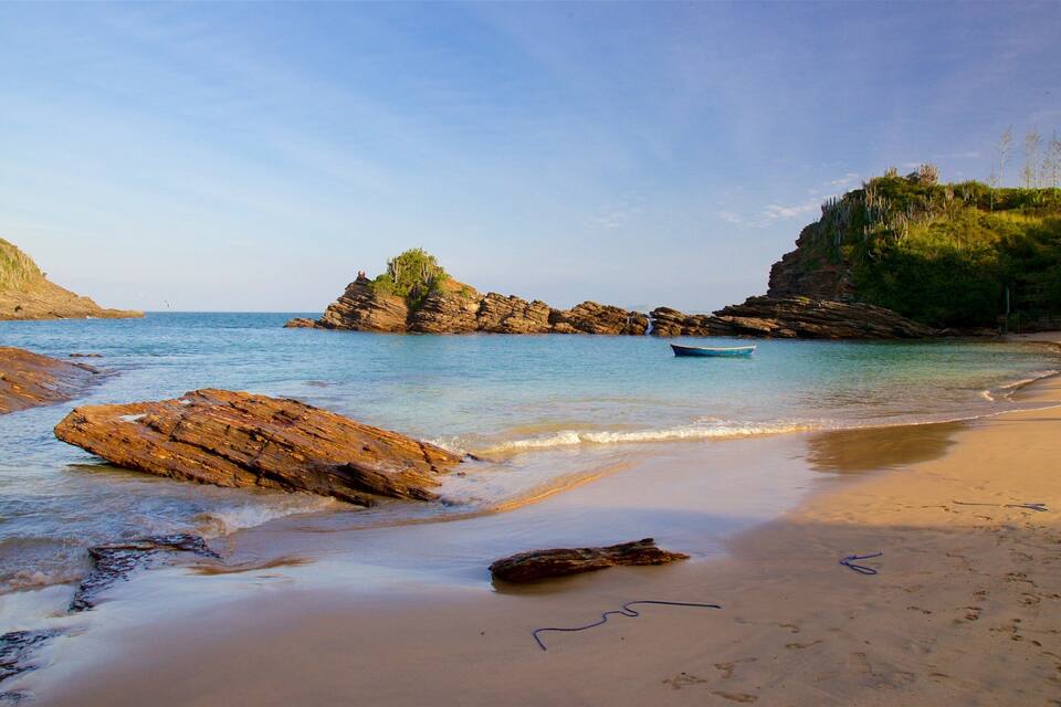 Paesaggio costiero con spiaggia sabbiosa, rocce affioranti e una piccola barca su acque calme.