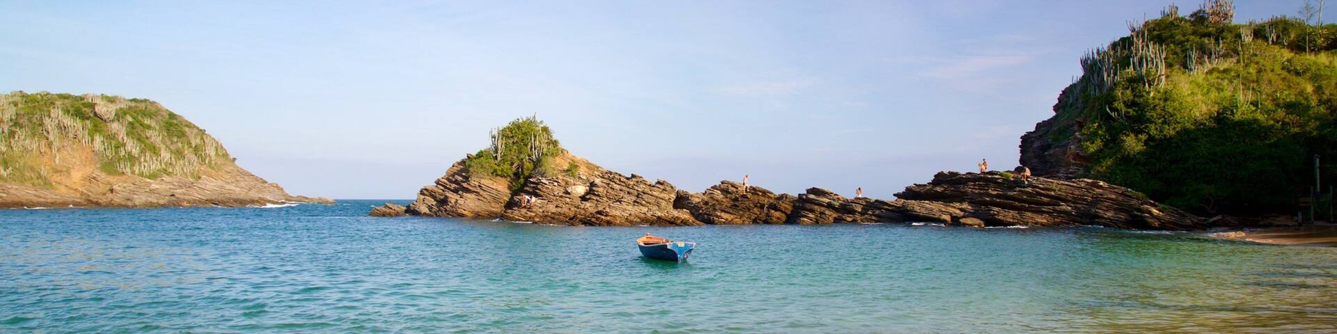 A calm sea with a small boat, rocky cliffs, and clear skies.