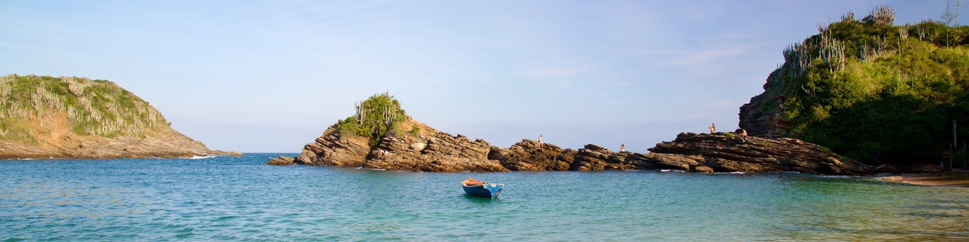 A calm sea with a small boat, rocky cliffs, and clear skies.