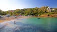 A beach with clear turquoise water, a row of boats, and a few people.