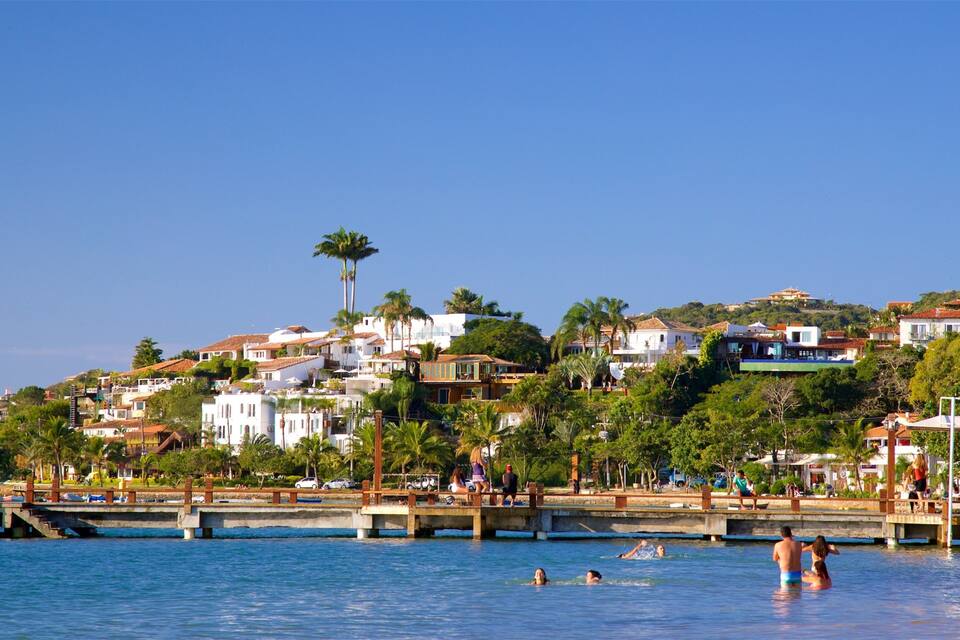 A coastal town with white buildings, palm trees, and people swimming in the water.