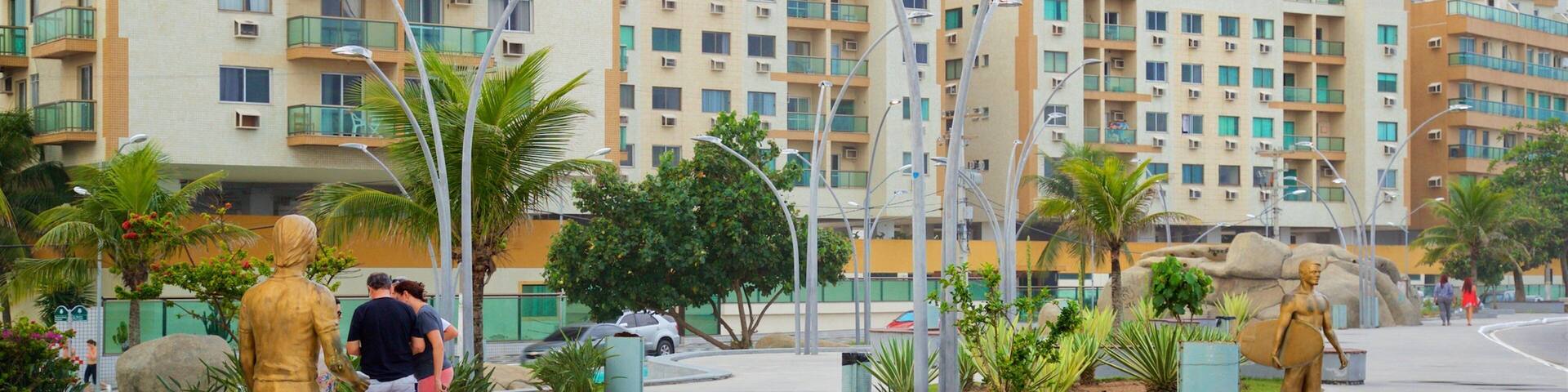 A public square with statues, palm trees, and modern apartment buildings in the background.