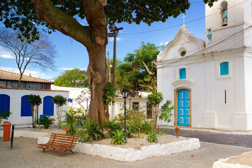 A white church with a blue door and a bell tower, surrounded by trees and a cobblestone street.