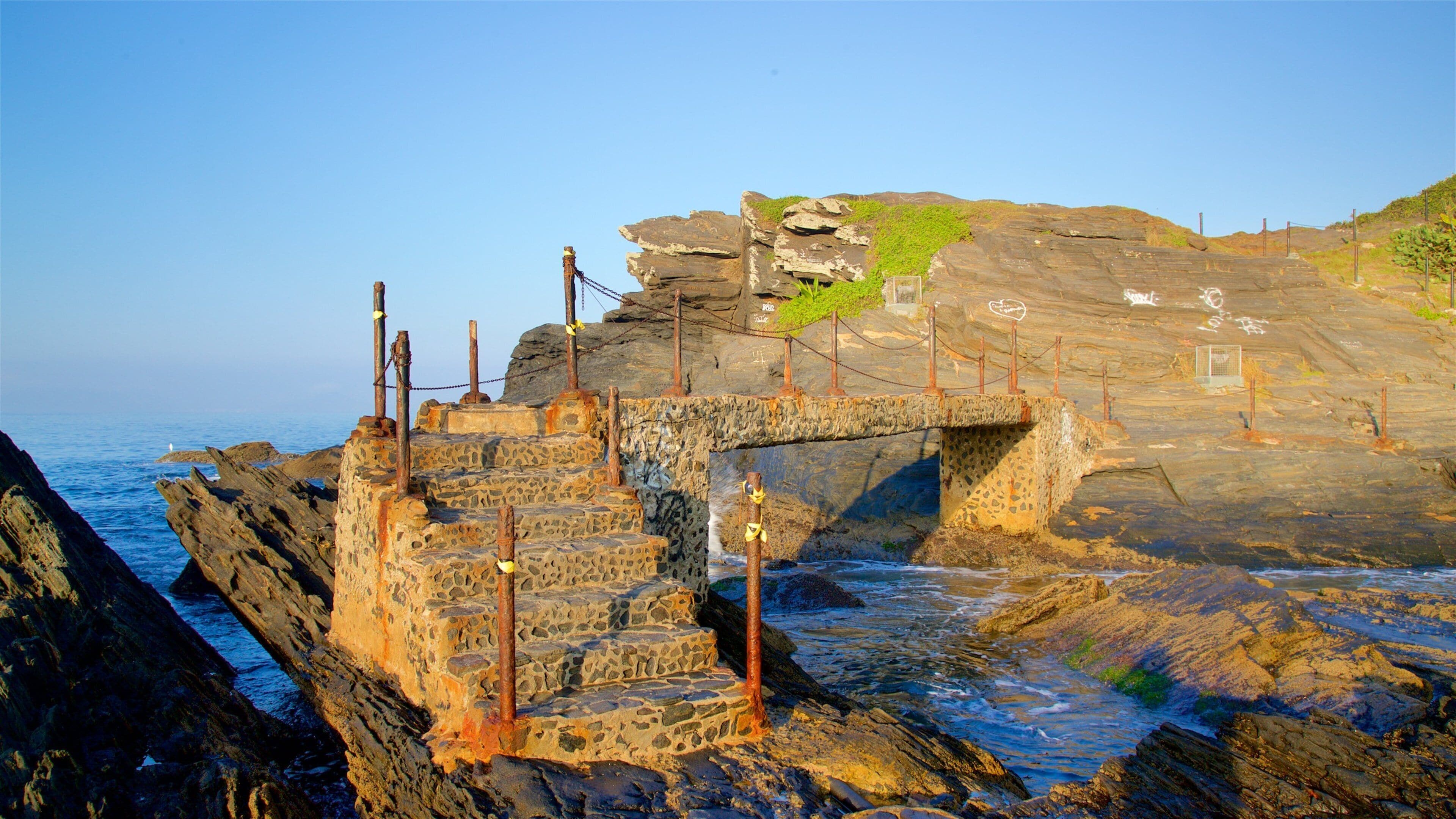 A coastal stone structure with rusted metal poles and a small bridge.
