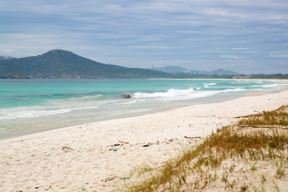 Una playa con agua turquesa cristalina, arena blanca y una colina distante con una torre.
