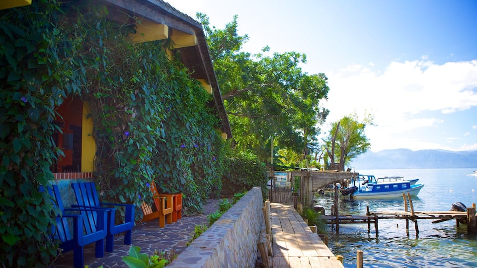 A wooden dock extending into a calm lake, with boats docked and a building with blue chairs and tables on the left.