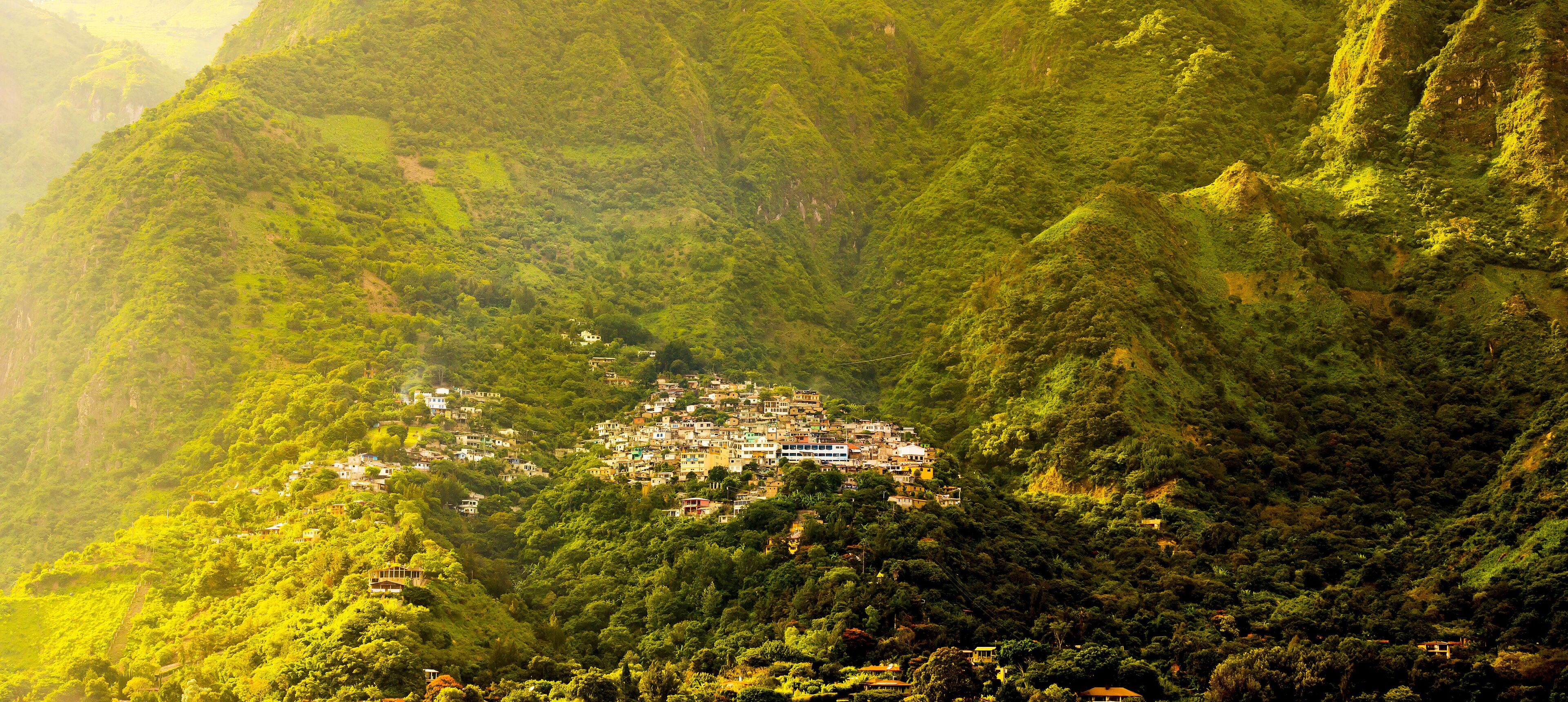 Uma aldeia aninhada num vale exuberante, rodeada por montanhas íngremes e florestadas.