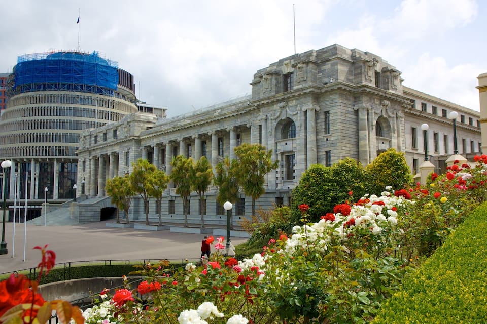 Un edificio histórico de arquitectura clásica, rodeado por un jardín bien cuidado con diversas plantas florecientes.