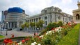 A historic building with classical architecture, surrounded by a well-maintained garden with various flowering plants.