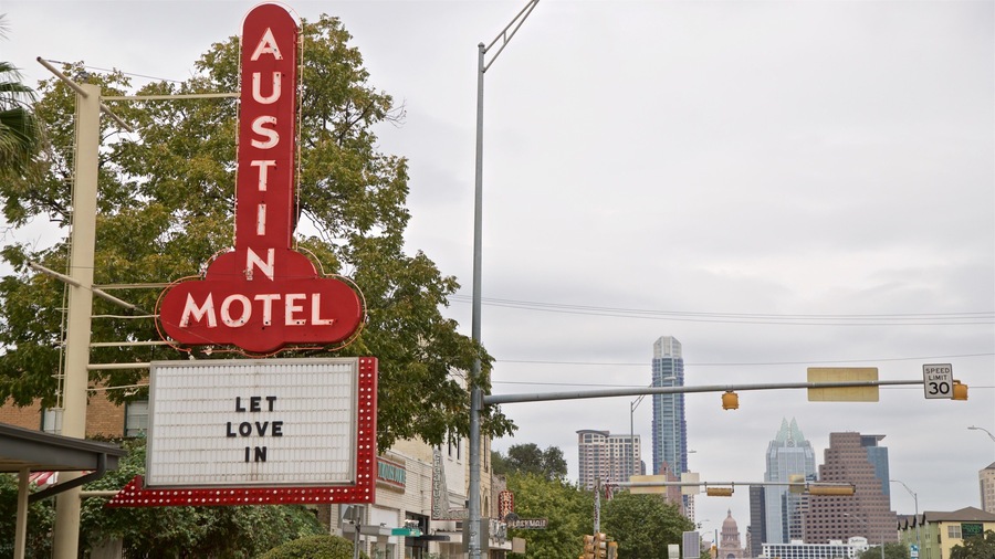A motel sign with "AUSTIN M" and "LET LOVE IN" text, a city skyline, and a speed limit sign of 30 in the background.