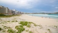 A sandy beach with waves, a lifeguard stand, and buildings in the background.