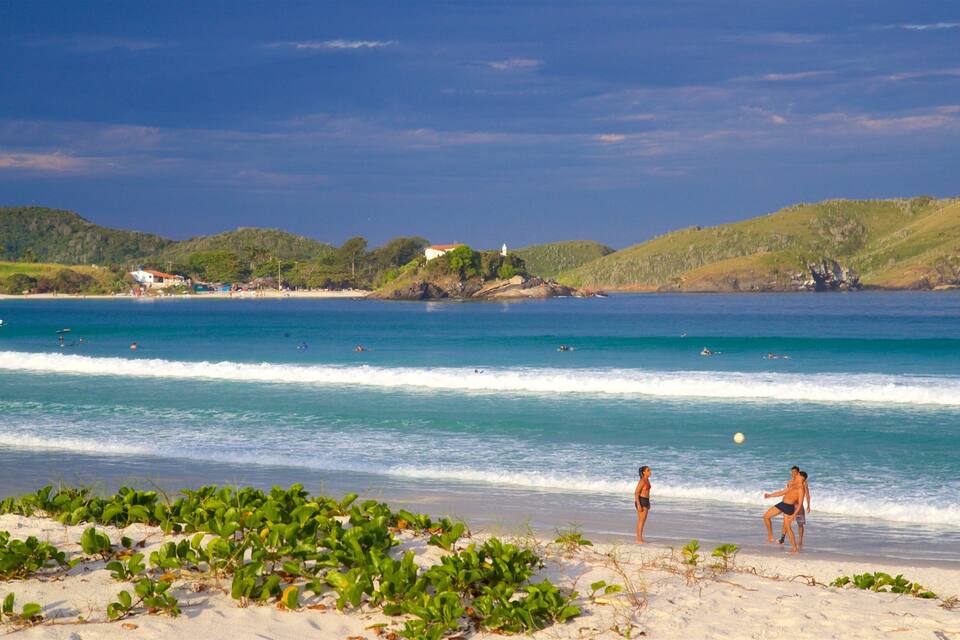 A beach with clear turquoise waters, a sandy shore, and green hills in the background.