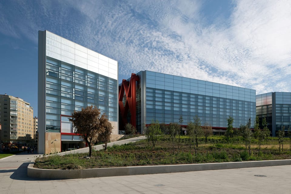 Een modern gebouw met grote glasramen en een rode constructie ervoor.