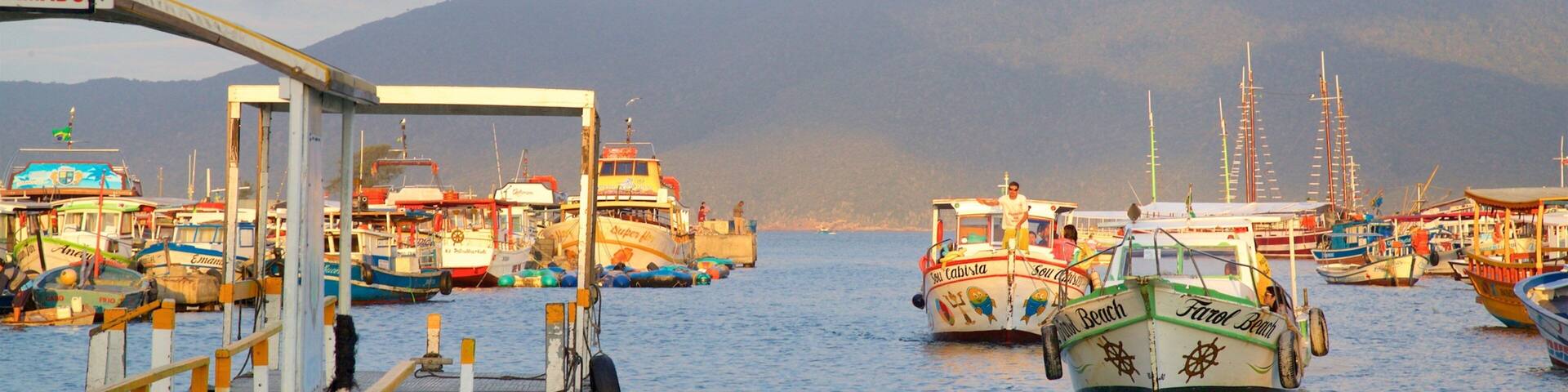 A marina with multiple boats docked, a pier, and mountains in the background.