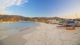 Una playa con barcos, una orilla arenosa y colinas al fondo.