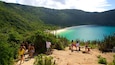 A coastal landscape with a sandy beach, turquoise waters, and lush green hills.