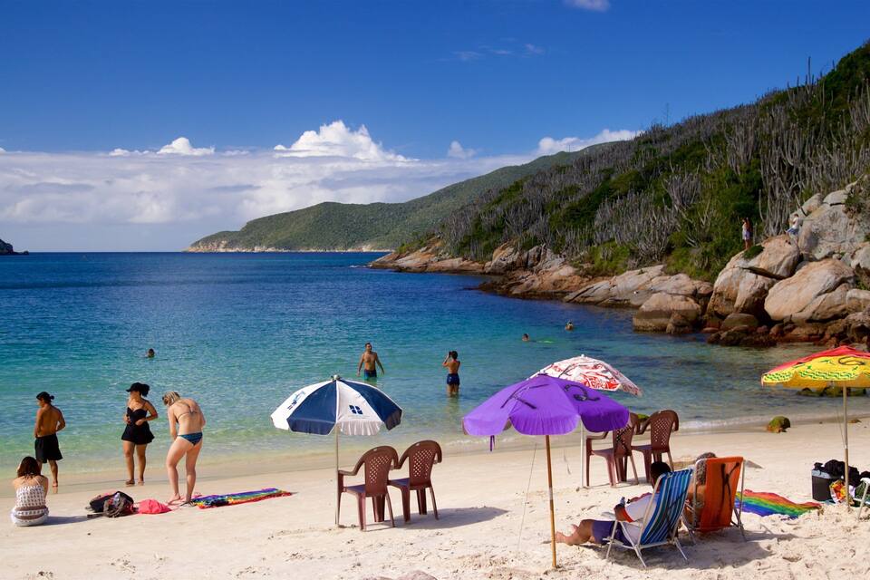 Una playa con agua turquesa cristalina, gente tomando el sol y sombrillas.