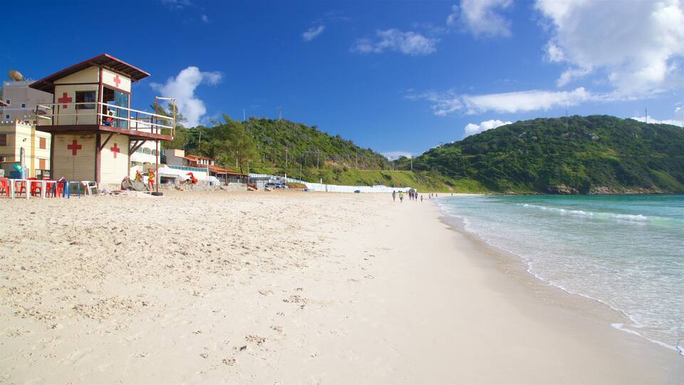 A beach with a lifeguard tower, clear turquoise waters, and a hilly backdrop.