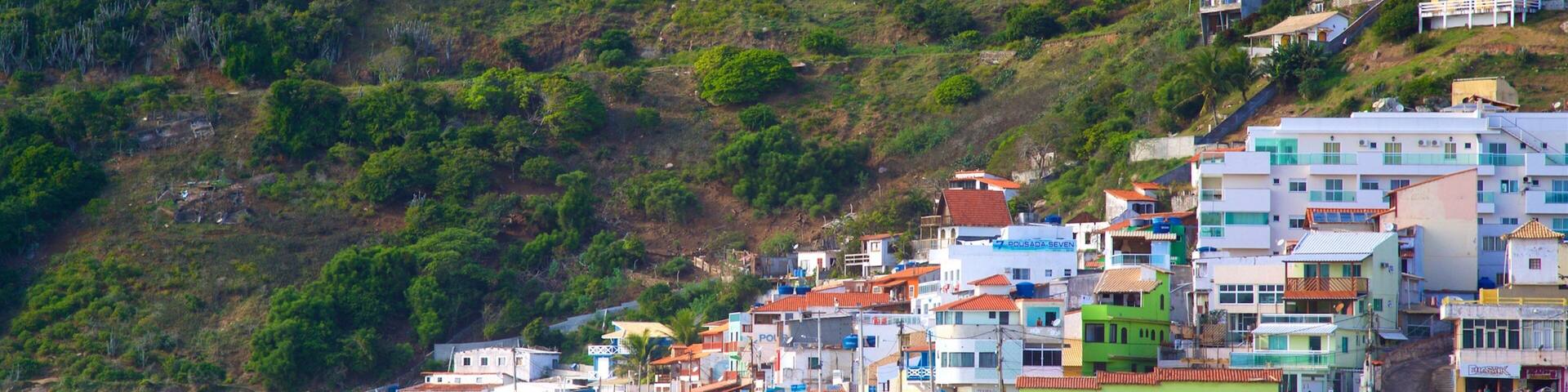 A coastal town with colorful buildings, a sandy beach, and a hillside with greenery.