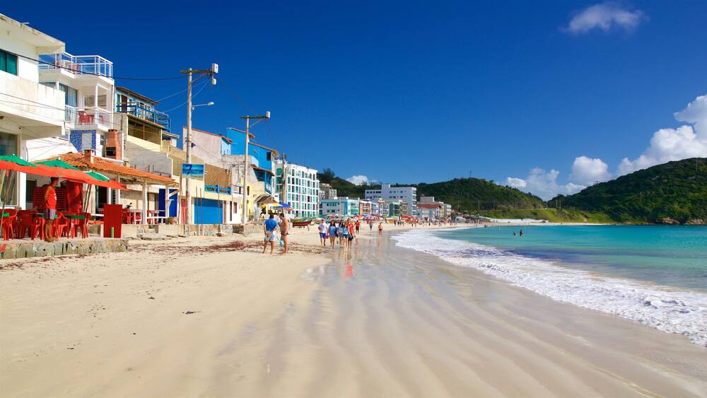 Ein Strand mit klarem türkisblauem Wasser, sandigem Ufer und bunten Gebäuden entlang der Küste.
