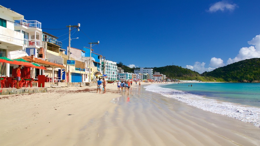 Uma praia com águas turquesa cristalinas, areal arenoso e edifícios coloridos ao longo da costa.