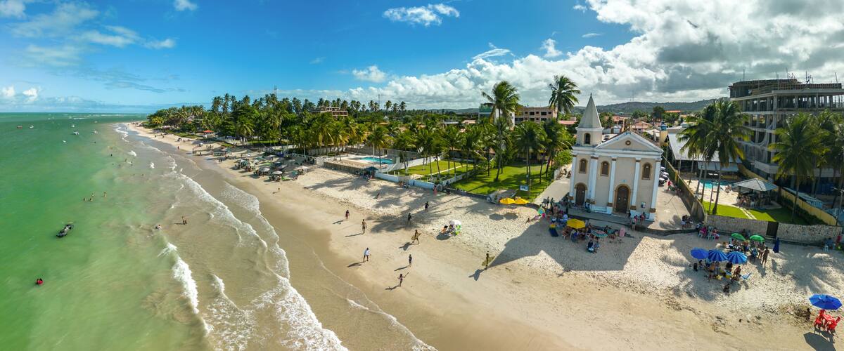 A beach with palm trees, a church, and a clear blue sky.