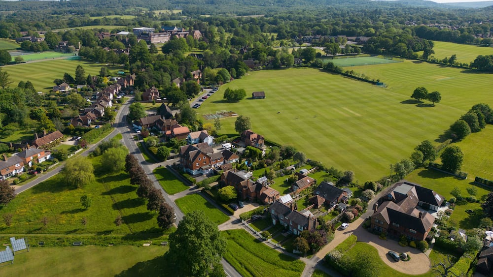 An aerial view of a rural village with houses, green fields, and a large estate.