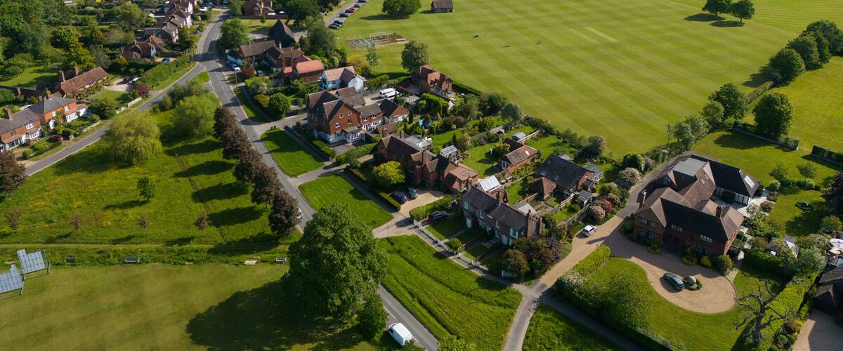 An aerial view of a rural village with houses, green fields, and a large estate.